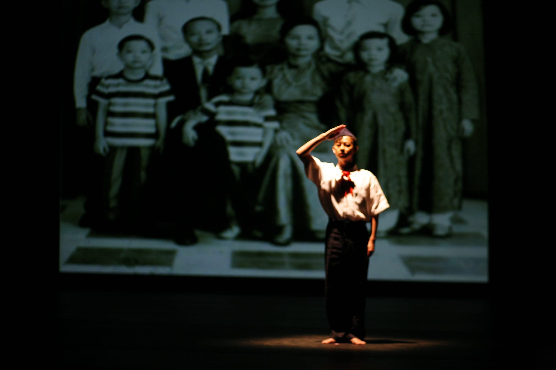 Minh stands on stage saluting with a photo of his Vietnamese ancestors projected on the wall