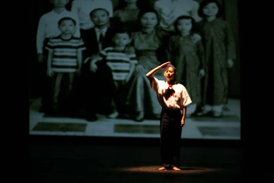 Minh stands on stage saluting with a photo of his Vietnamese ancestors projected on the wall