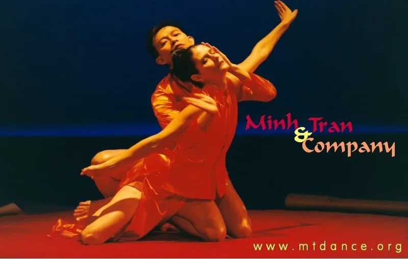 Minh on stage in orange intertwined with another dancer in orange.